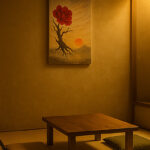畳の和室に掛けられた額無しキャンバス画。赤い花を咲かせた樹と沈む夕陽が描かれ、温かな灯りに包まれている。