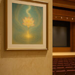 コンサートホールの壁に額装された黄金色の蓮の写意画。温かな光に包まれ、舞台と客席を背景に幻想的な雰囲気を演出している。