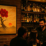 レンガの壁に赤い花と夕日の写意画が掛けられ、カウンター越しに人々が会話を楽しむレストランまたはバーの様子