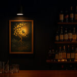 バーカウンターの壁に飾られた写意画と照明、周囲にはボトル棚が並ぶ様子